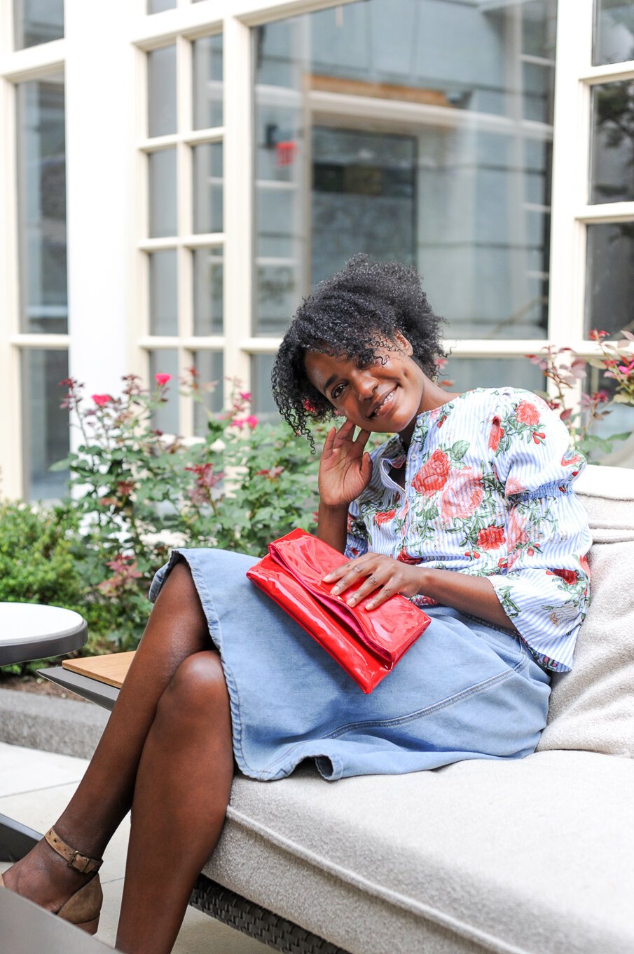 Zoë in a floral blouse and denim skirt relaxing on a garden sofa